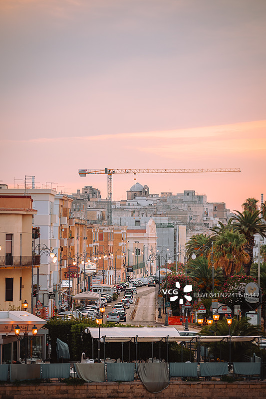 夕阳下熙熙攘攘的城市街道的鸟瞰图，有建筑、汽车和棕榈树，天空色彩斑斓，地点为意大利塔兰托。图片素材