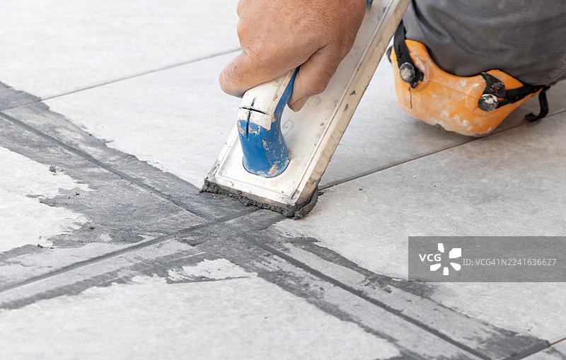 特写：一个人用橡胶抹子给地板瓷砖填缝，展示了施工过程和对细节的关注图片素材