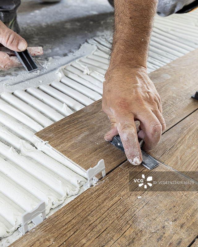 一名木匠在工作室里，使用粘合剂和垫片安装木纹地板砖的特写图片素材