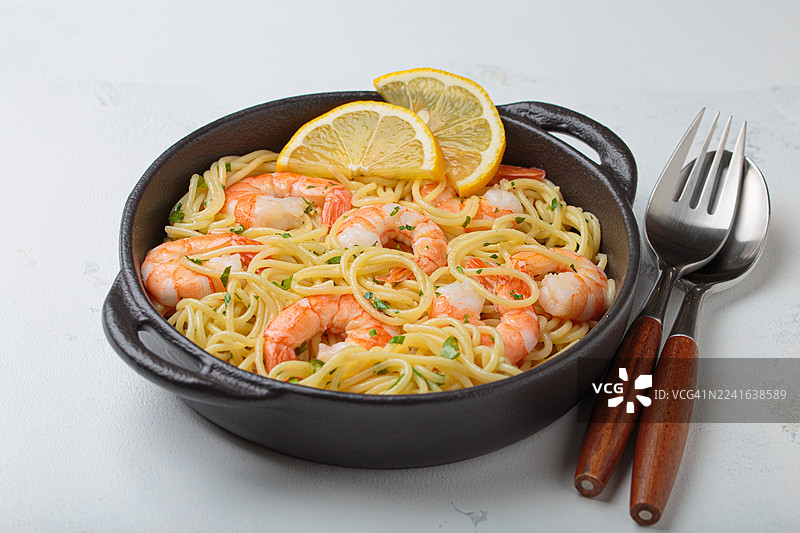白色餐桌上黑色碗里的美味鲜虾意大利面，配有柠檬片，俯视角度，准备上桌图片素材