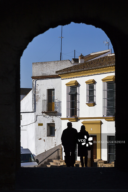 一对情侣背对镜头，站在窗前，背景是西班牙卡蒙纳迷人的欧洲村庄，拱门构图。图片素材