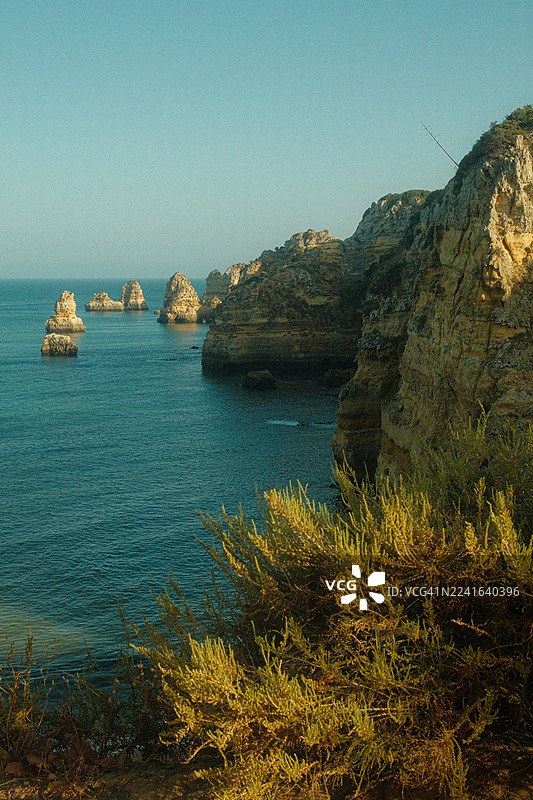 晴朗天空下，戏剧性的海岸悬崖和海蚀柱从宁静的蓝色海洋中升起，葡萄牙，拉各斯图片素材
