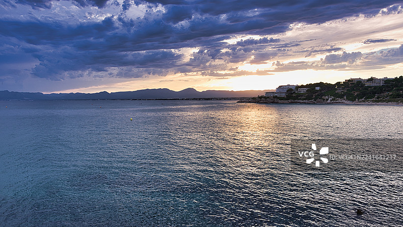 夕阳时分，戏剧般的天空映衬着海景，远处可见山峦和海岸建筑，地点：萨洛，西班牙，萨洛角图片素材