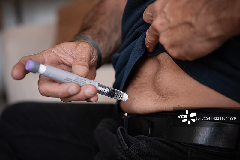 一位成熟的糖尿病患者在家里地向腹部注射胰岛素图片素材