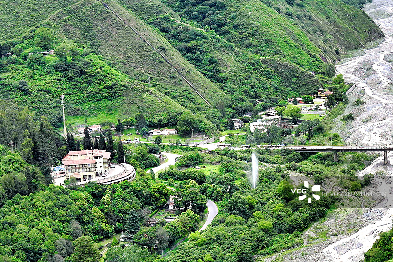 高角度拍摄的郁郁葱葱的绿色山地景观，河水、桥梁和建筑坐落其中图片素材