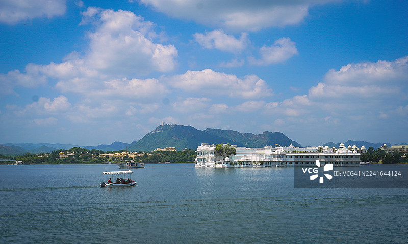 印度的吉尔瓦，皮丘拉湖，湖上有船只，背景是山脉和带有云朵的蓝天，远处有一座白色宫殿的风景。图片素材