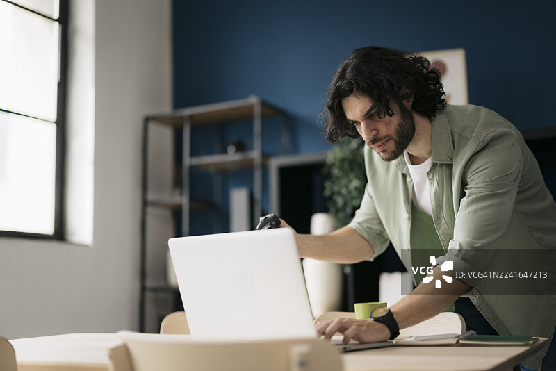 年轻男性摄影师在家里的办公室使用笔记本电脑工作图片素材