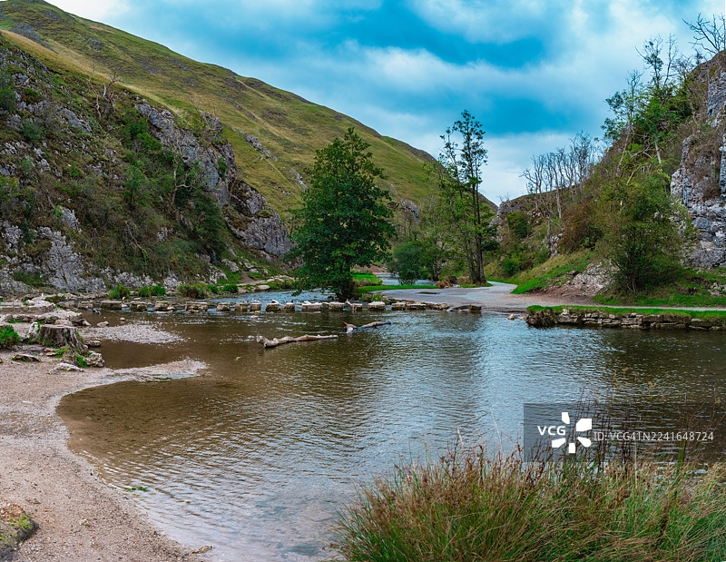 英国阿什伯恩，多夫代尔石桥，河畔风光，树林环绕，云层密布的天空图片素材