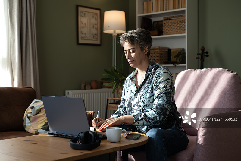 戴眼镜的女子在家对着笔记本电脑购物，面带微笑图片素材