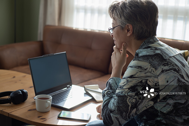 戴眼镜的女士在家对着笔记本电脑购物，面带微笑，表情积极图片素材