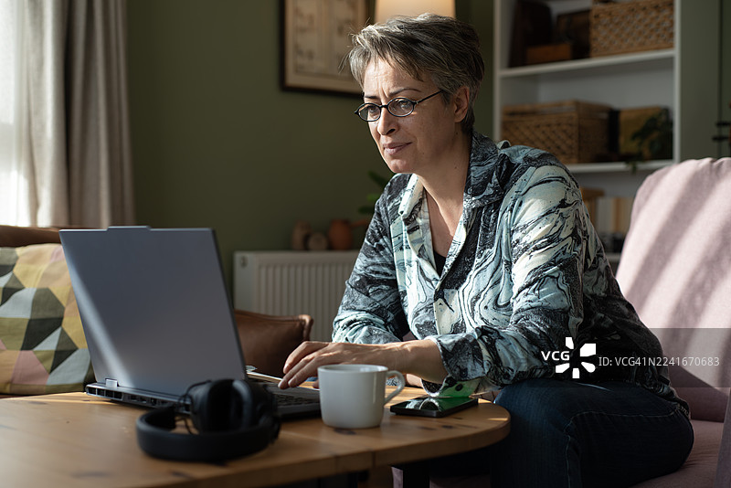 戴眼镜的女士在家用笔记本电脑购物，面带微笑图片素材