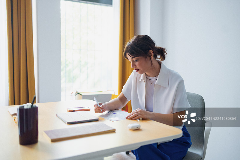 现代家庭办公室里，专注的女性在明亮的办公桌前工作，桌上有文件、电话和笔记本。图片素材