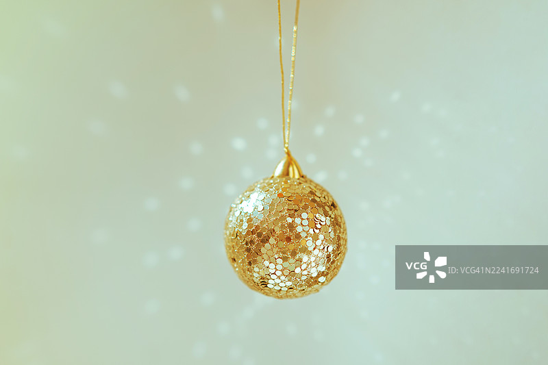 金色亮片圣诞装饰品悬挂在柔和、闪烁的光线下，营造节日氛围图片素材
