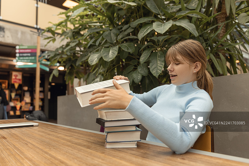 一位漂亮的金色头发的十几岁女学生在图书馆学习图片素材