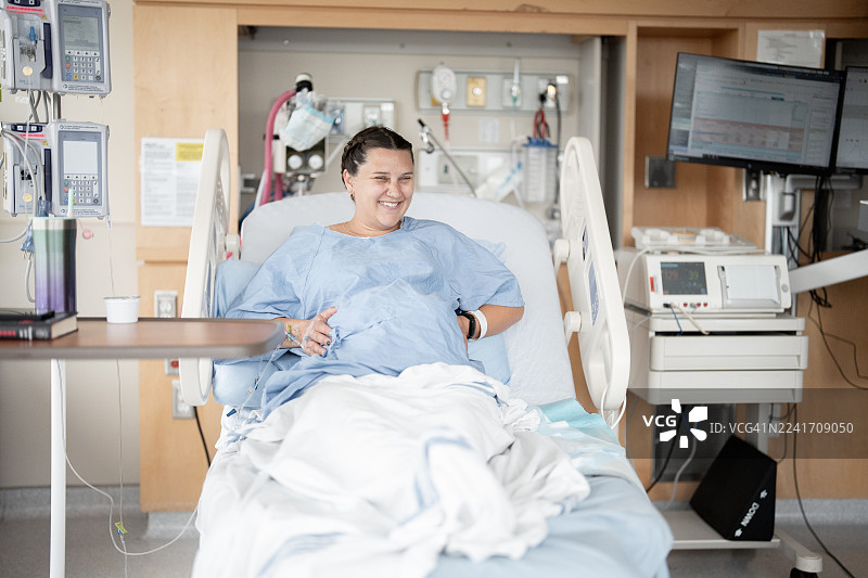 快乐的产妇在分娩时躺在医院病床上，一位西班牙裔女性在现代产房中微笑图片素材