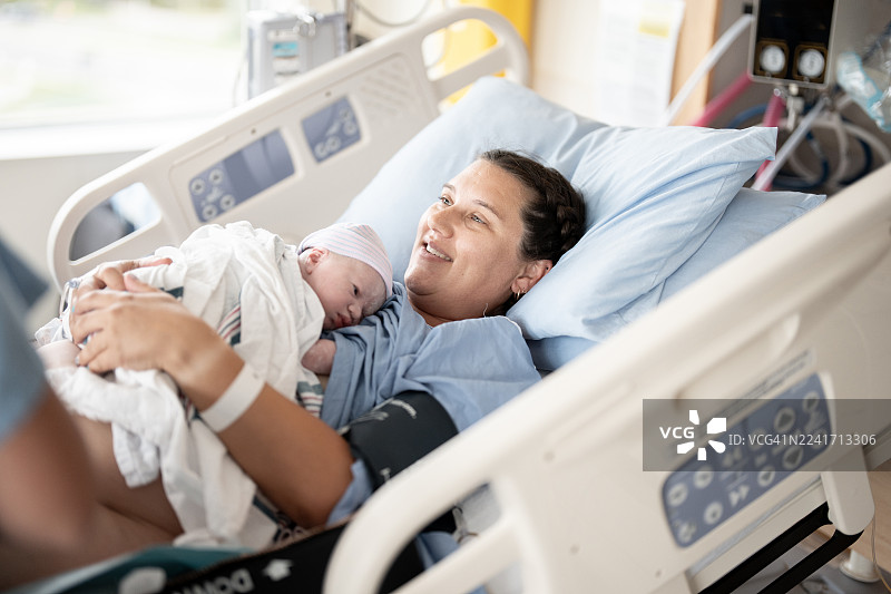 产后在医院病床上，快乐的新手妈妈抱着新生儿图片素材