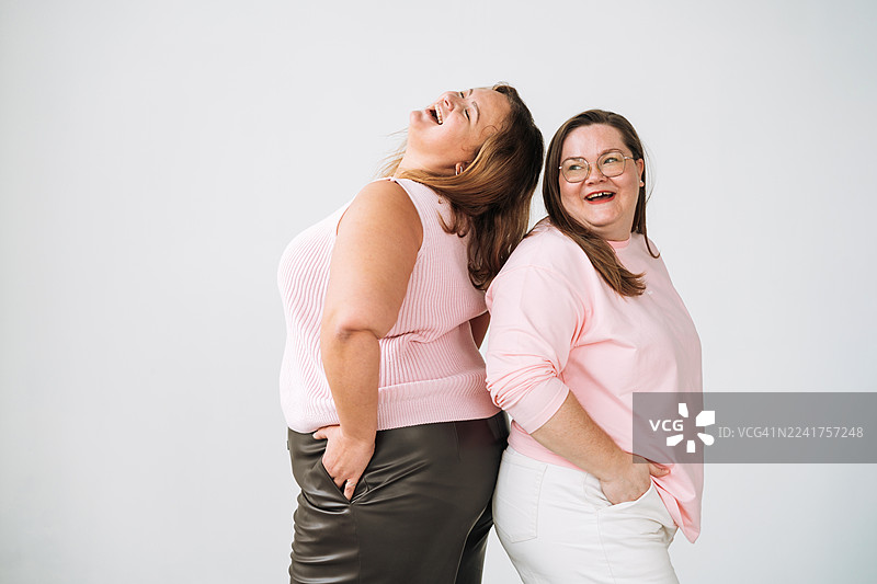 两位快乐的大码女性在白色工作室背景下大笑，展现身体积极性和愉悦的友谊图片素材