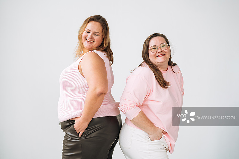 两位快乐的大码女性在白色工作室背景下大笑，展现身体积极性和欢乐的友谊图片素材