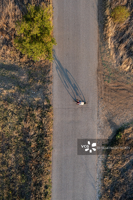乡村道路上骑自行车的人的鸟瞰图，有长长的影子和金色时段的光线图片素材