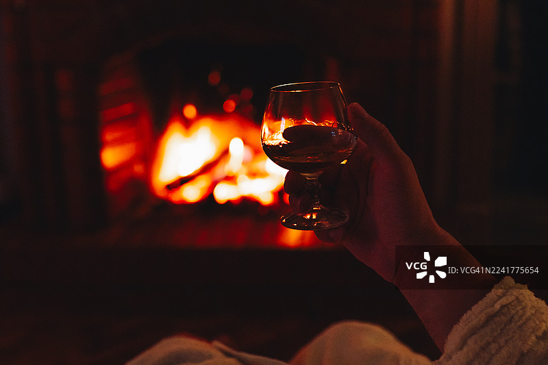 手持白兰地酒杯，在温暖的壁炉旁放松图片素材