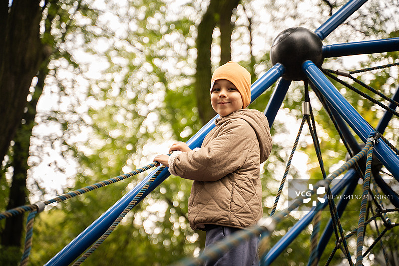 快乐的男孩在秋天的公园里玩绳索攀爬架图片素材