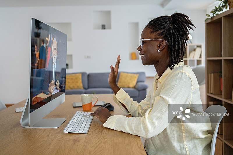 一位年轻的黑人女商人在家参加在线会议，对着笔记本电脑挥手微笑图片素材