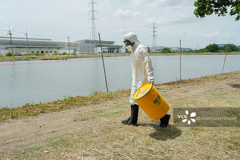 生态学家穿着防护服，在养殖水生动物的农场池塘中检查水质，并采集水样进行分析。图片素材