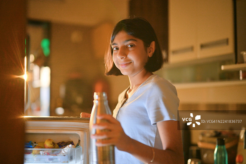 十几岁的女孩在厨房从冰箱里拿水瓶图片素材
