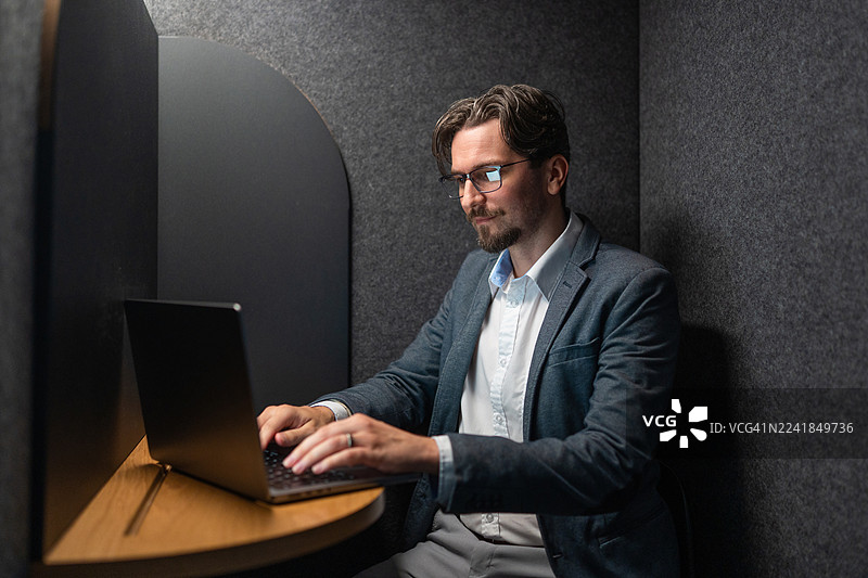 专注的中年白人商务人士在办公室隔间里用笔记本电脑打字图片素材