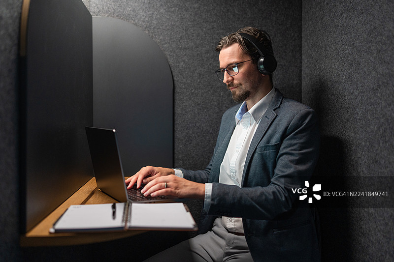 专注的商人在私人办公隔间里用笔记本电脑工作图片素材