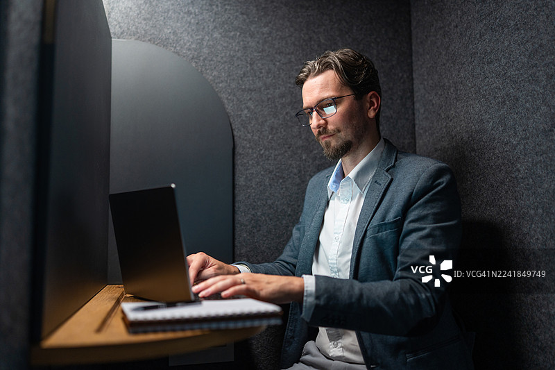 专注的商人在私人办公室隔间里用笔记本电脑打字图片素材