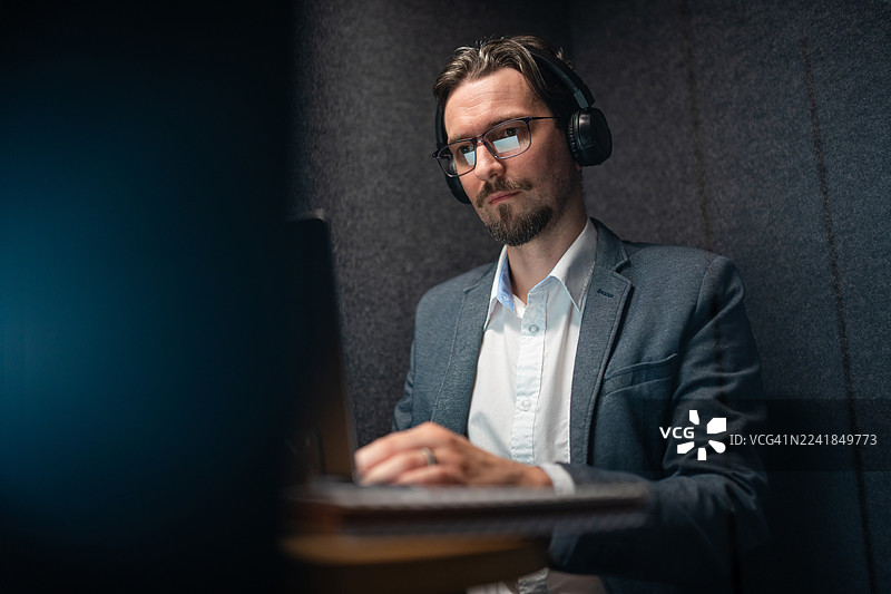 戴着耳机专注工作的商务人士在安静的办公室隔间里图片素材