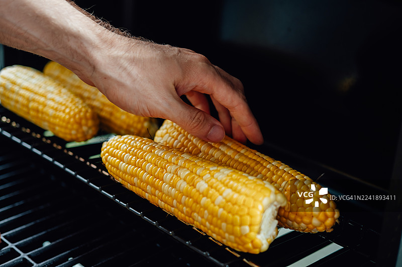手在烧烤架上调整玉米棒图片素材