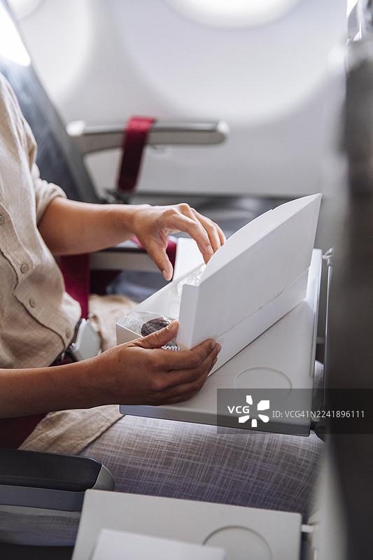 乘客坐在飞机座位上打开机上零食盒，温馨的旅途瞬间图片素材