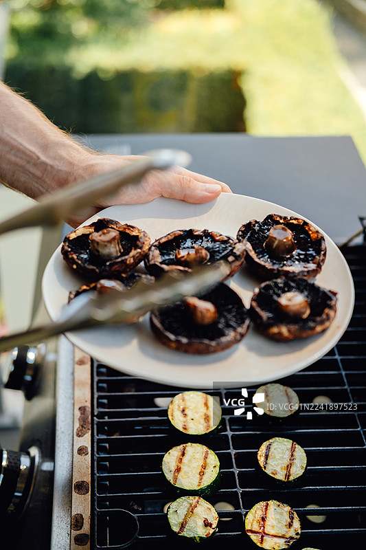 用夹子从烤架上取出烤好的波多贝罗蘑菇图片素材
