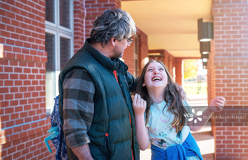 10岁女儿在砖砌的学校走廊里和爸爸分享欢笑图片素材