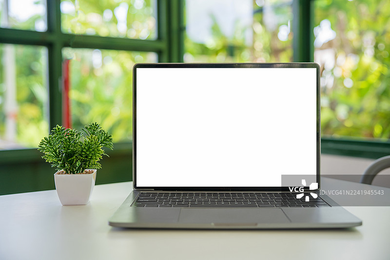 咖啡馆背景的桌子上放着一台屏幕空白的笔记本电脑。笔记本电脑屏幕带有复制空间。舒适的工作场所。正面视图。网上冲浪。视频会议。在线购物。图片素材