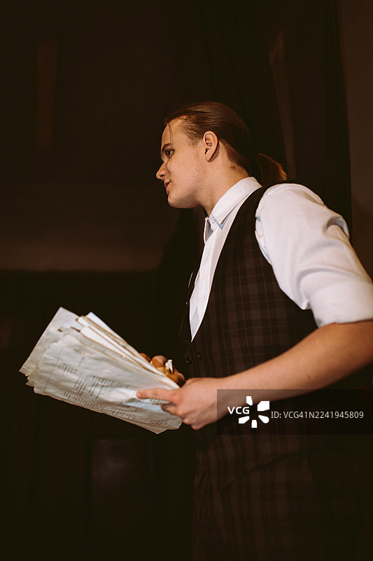 演员在戏剧表演中手持剧本站在舞台上，身穿格子背心和白衬衫图片素材