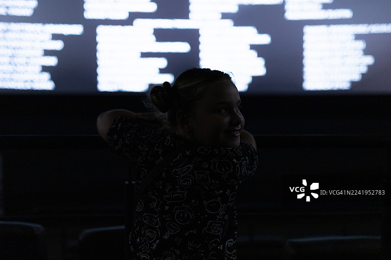 身着剪影的女孩在黑暗房间里享受投影屏幕的氛围，营造出一种忧郁而俏皮的瞬间图片素材