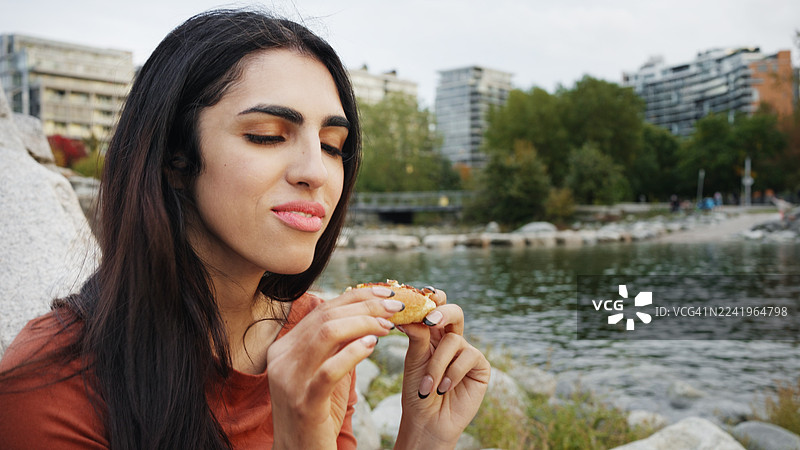 一位迷人的女性在户外水边和城市景观旁享用披萨图片素材