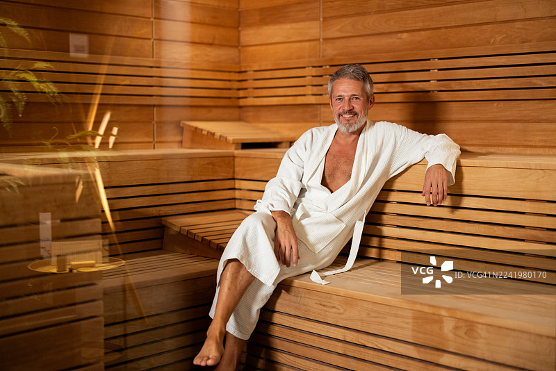 放松的成熟男子在桑拿房穿着白色浴袍图片素材