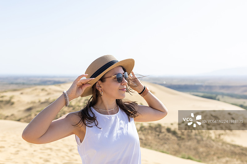 戴着草帽和太阳镜的女士在阳光明媚的日子里享受沙漠沙丘图片素材