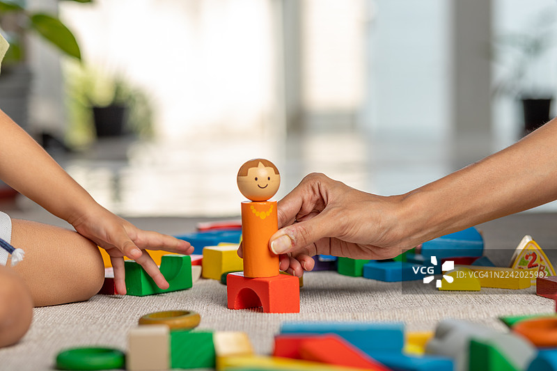 一个孩子在柔软的地毯上玩着色彩鲜艳的积木，一位成年人在旁协助，一起搭建有趣的建筑图片素材