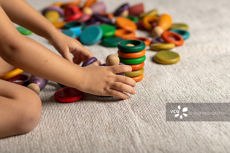 孩子在柔软的地垫上玩耍，堆叠着色彩鲜艳的木制圆盘图片素材