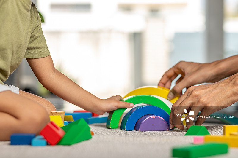 白天，在明亮的室内空间，一个幼儿正在玩色彩鲜艳的木制积木，进行有趣的搭建活动。图片素材
