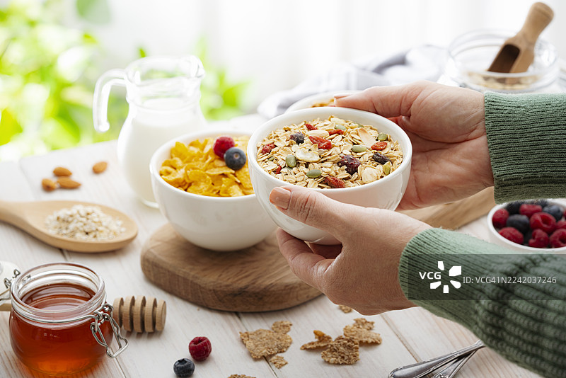 女性双手在桌上捧着一碗装满格兰诺拉麦片、干果和种子的碗。早餐谷物或健康饮食与节食。高膳食纤维食品图片素材