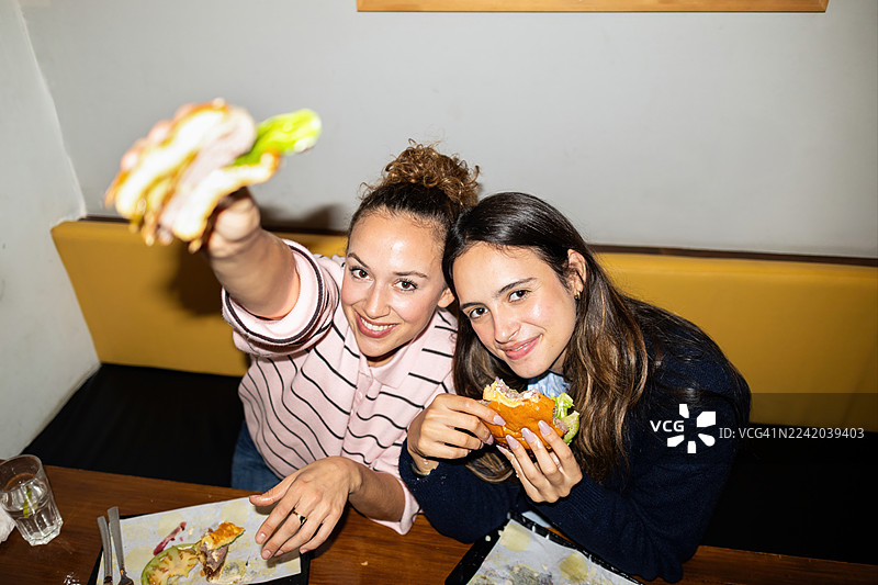 一群女性朋友在餐厅里笑着吃汉堡，用闪光灯捕捉欢乐的瞬间，庆祝友谊图片素材