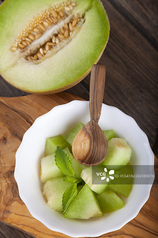白盘中切好的甜瓜放在乡村木桌的木质砧板上。图片素材