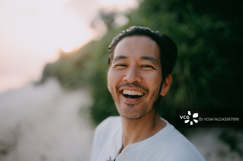 日落时分，一个男人在海滩上对着镜头大笑图片素材