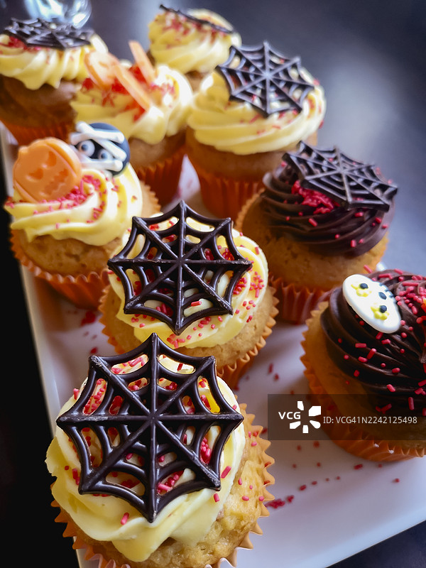 万圣节纸杯蛋糕，装饰有巨大的巧克力蜘蛛网，俯视视角，深色背景图片素材